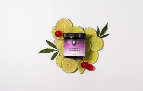 A jar of Sleep CBD Gummies+ Cherry Limeade flavor placed on a bed of lime slices and cherries,