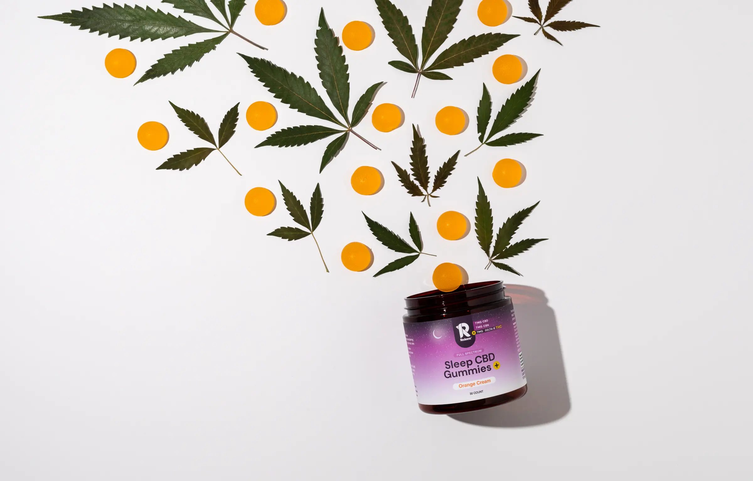 A jar of Sleep CBD Gummies+ (Orange Cream flavor) surrounded by cannabis leaves and orange gummies