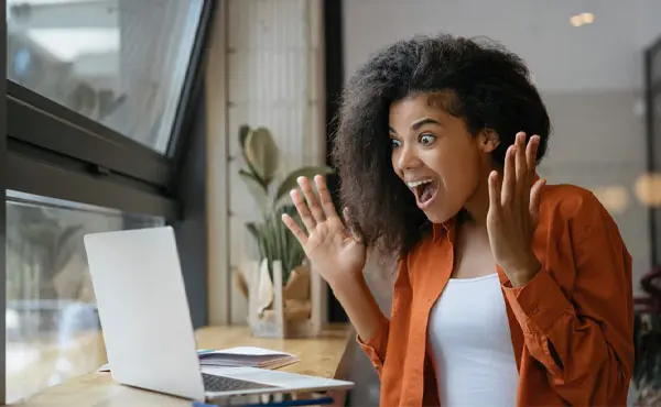  Image features a woman excitedly reacting to something on her laptop.