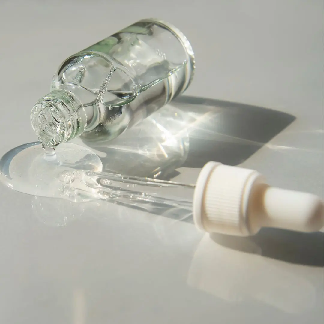 A clear glass bottle with clear liquid spilling onto a light surface A clear glass bottle with clear liquid spilling onto a light surface